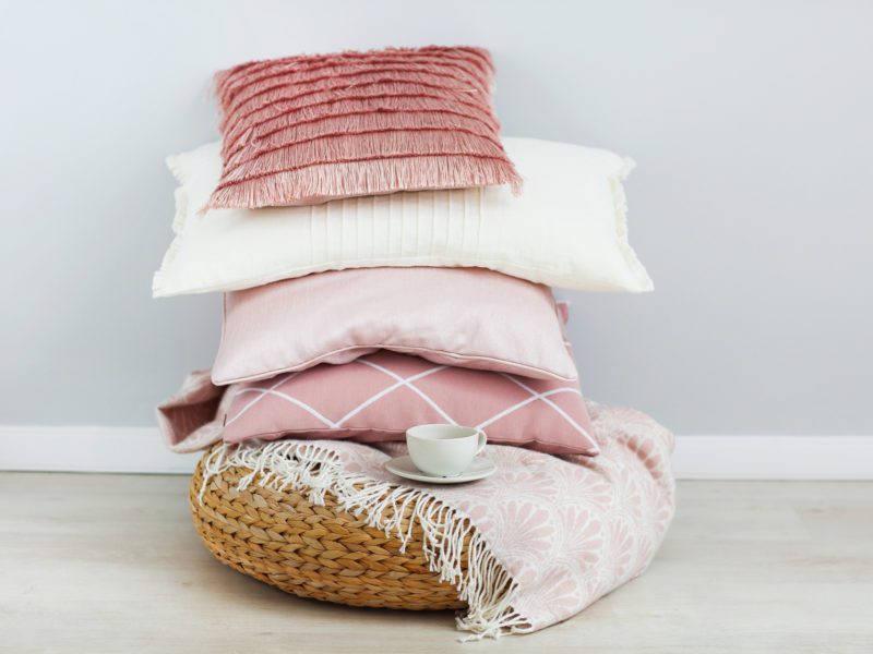 pink and white pillows on a rattan footstool